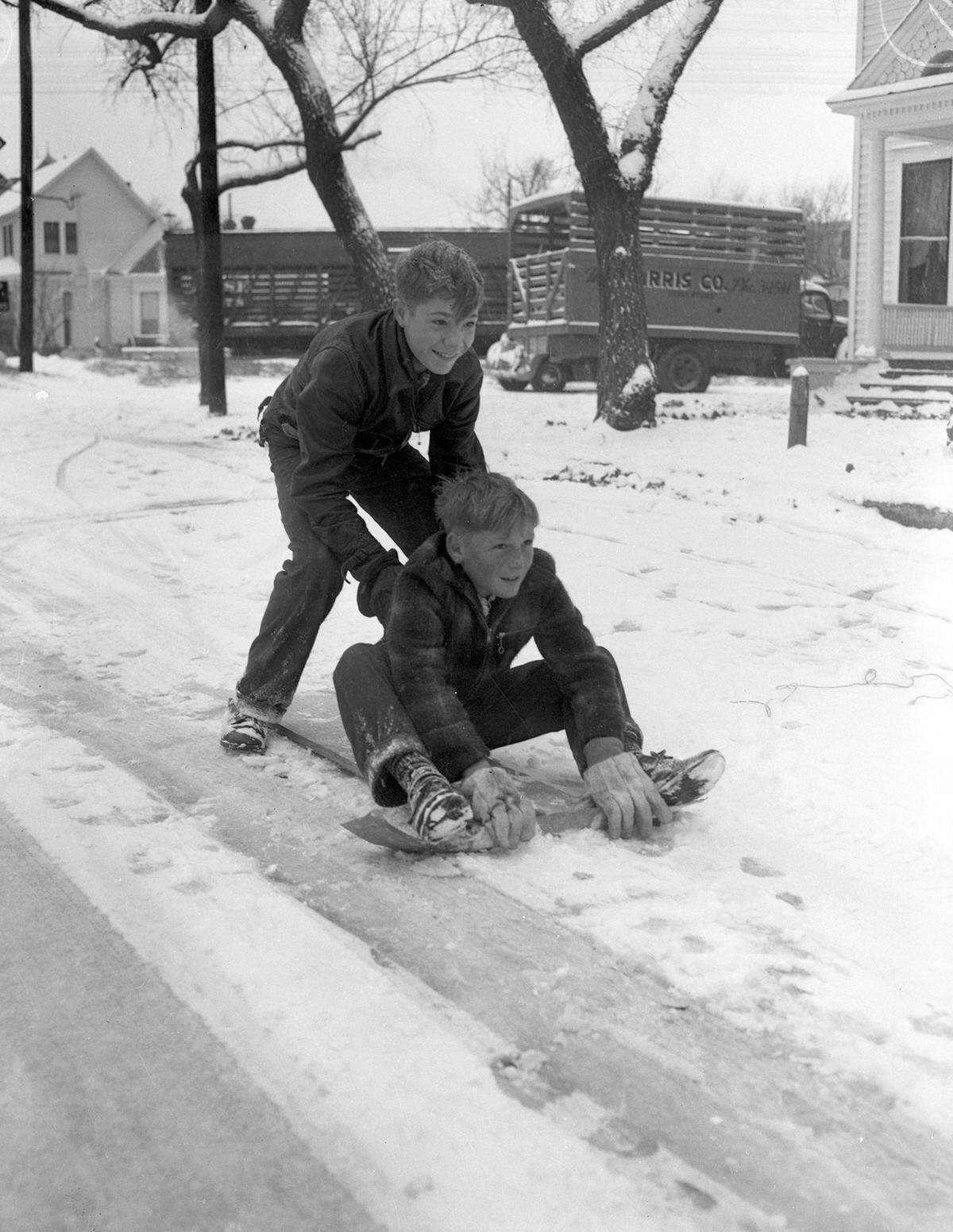 Dec. 31, 1946: “Harry McGrowan, 13, and his brother, Dennie, 9, riding on a snow sled. Harry is shown pushing his younger brother on a makeshift sled on the snow covered ground. Both are smiling and wearing coats, snow shoes and gloves. Behind them a few houses can be seen, along with trees and some trucks.”