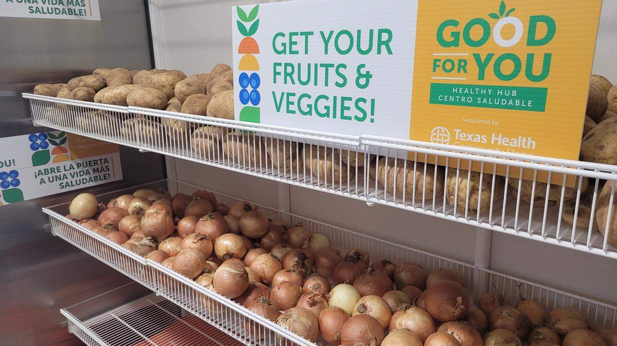 Russet potatoes and yellow onions are piled on shelves. At the top sits a sign that reads “Get your fruits & veggies!”