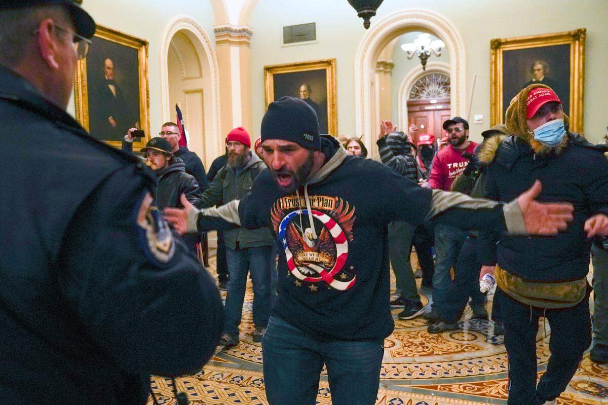 FILE - In this Jan. 6, 2021, file photo, Trump supporters gesture to U.S. Capitol Police in the hallway outside of the Senate chamber at the Capitol in Washington. Doug Jensen, an Iowa man at center, was jailed early Saturday, Jan. 9, 2021 on federal charges, including trespassing and disorderly conduct counts, for his alleged role in the Capitol riot. Jensen, 41, of Des Moines, was being held without bond at the Polk County Jail and county sheriff’s Sgt. Ryan Evans said he didn’t know if Jensen had an attorney. (AP Photo/Manuel Balce Ceneta, File)