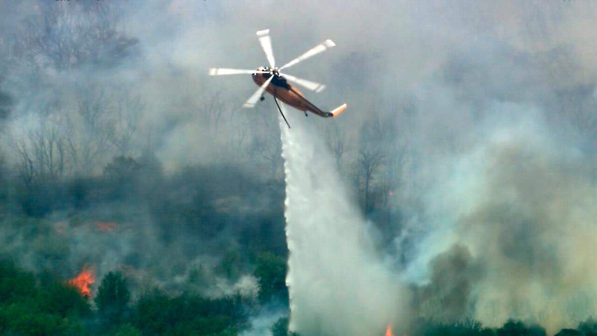 In this still taken from video, a helicopter dumps water on a wildfire in Palo Pinto County, Texas on Monday, July 18, 2022. The wildfire has burned several homes and resulted in about 300 homes being evacuated around Possum Kingdom Lake in North Texas amid sweltering temperatures and dry conditions, authorities said.