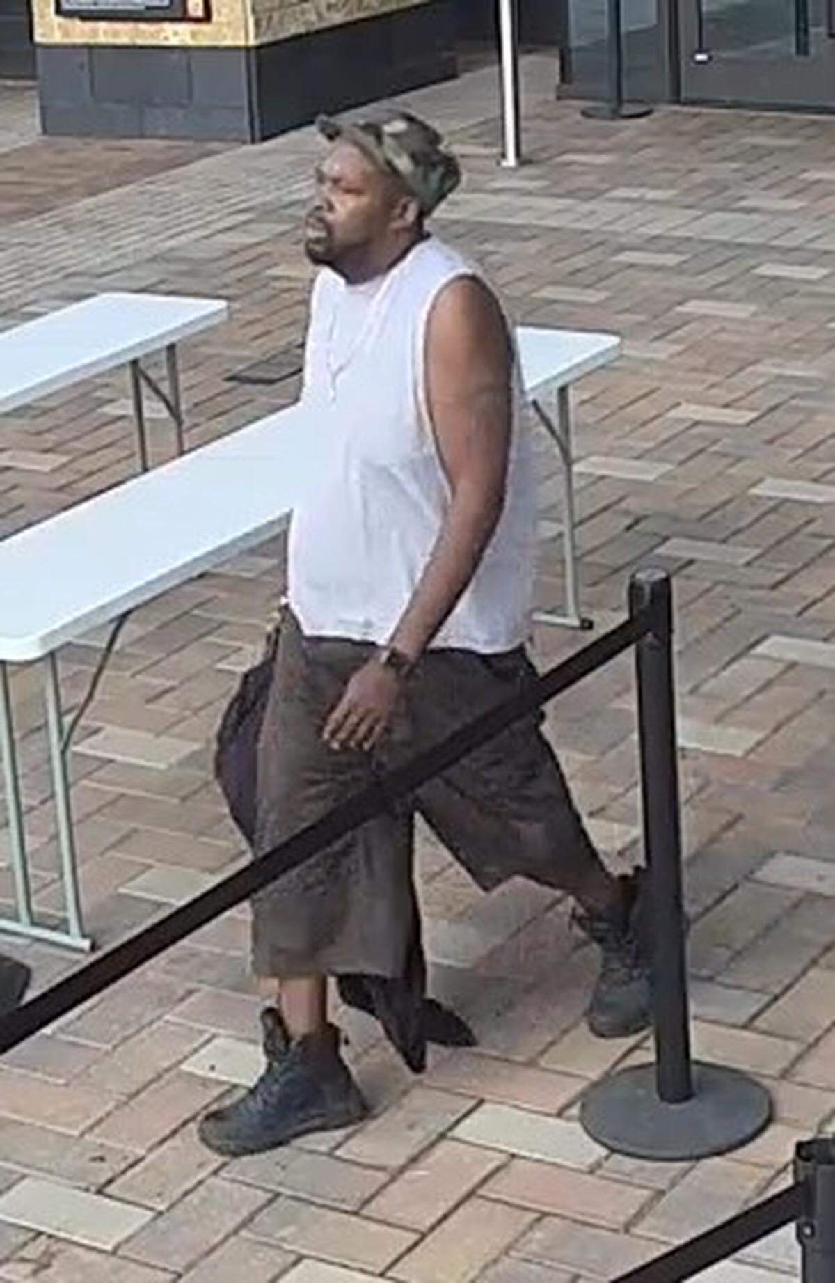 A man walking by a long white table with a black bundle in his hand.