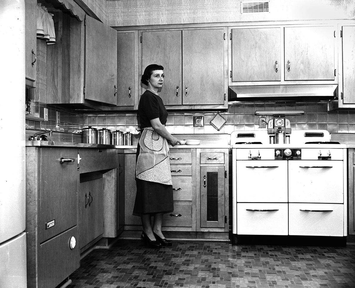 March 2, 1954: Maple-fronted cabinets give an elegant touch to the actual cooking end of the kitchen-den. Mrs. W. H. Granger finds the stainless steel tile above the drainboard especially easy to keep.