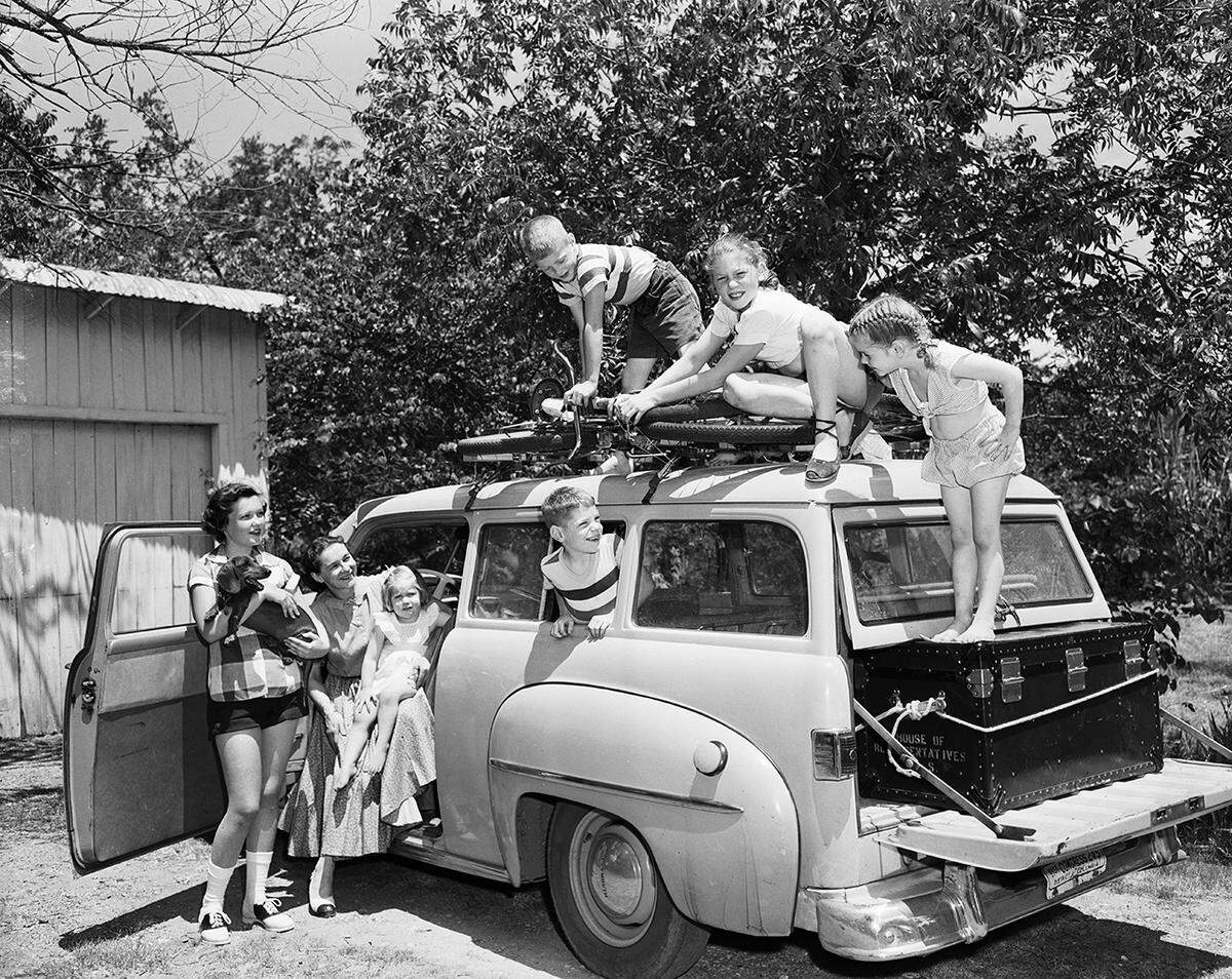 June 21, 1952: Arriving in Grapevine from Washington, D. C., the family of Congressman Wingate Lucas starts unpacking Saturday by removing four bicycles from the top of the car. Left to right are Mary Ann Clark, niece of Mrs. Lucas, holding the dog, Weinie; Mrs. Lucas, and the five Lucas children, Ellen, Will, Wink, Mary Dell and Christine.