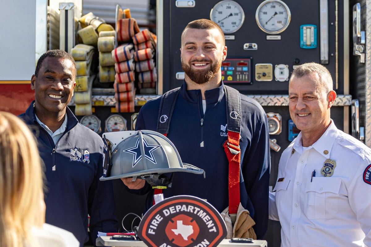 USAA Senior Vice President Rob Braggs, left, and Arlington Fire Chief Bret Stidham, right, take a photo with Dallas Cowboys tight end Jake Ferguson as he holds his custom made firefighter helmet during a Turkey Fryer Fire Safety demonstration at the Arlington Fire Department Training Facility Station 14 in Arlington on Tuesday, Nov. 14, 2024.
