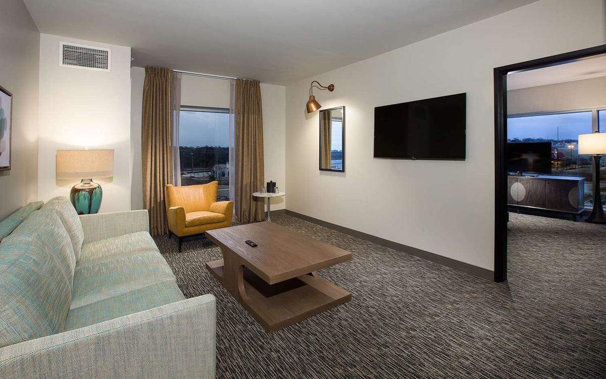 The living room of Southlake's Cambria hotel features a large couch, coffee table, accent chair and television with a window view of surrounding Southlake.