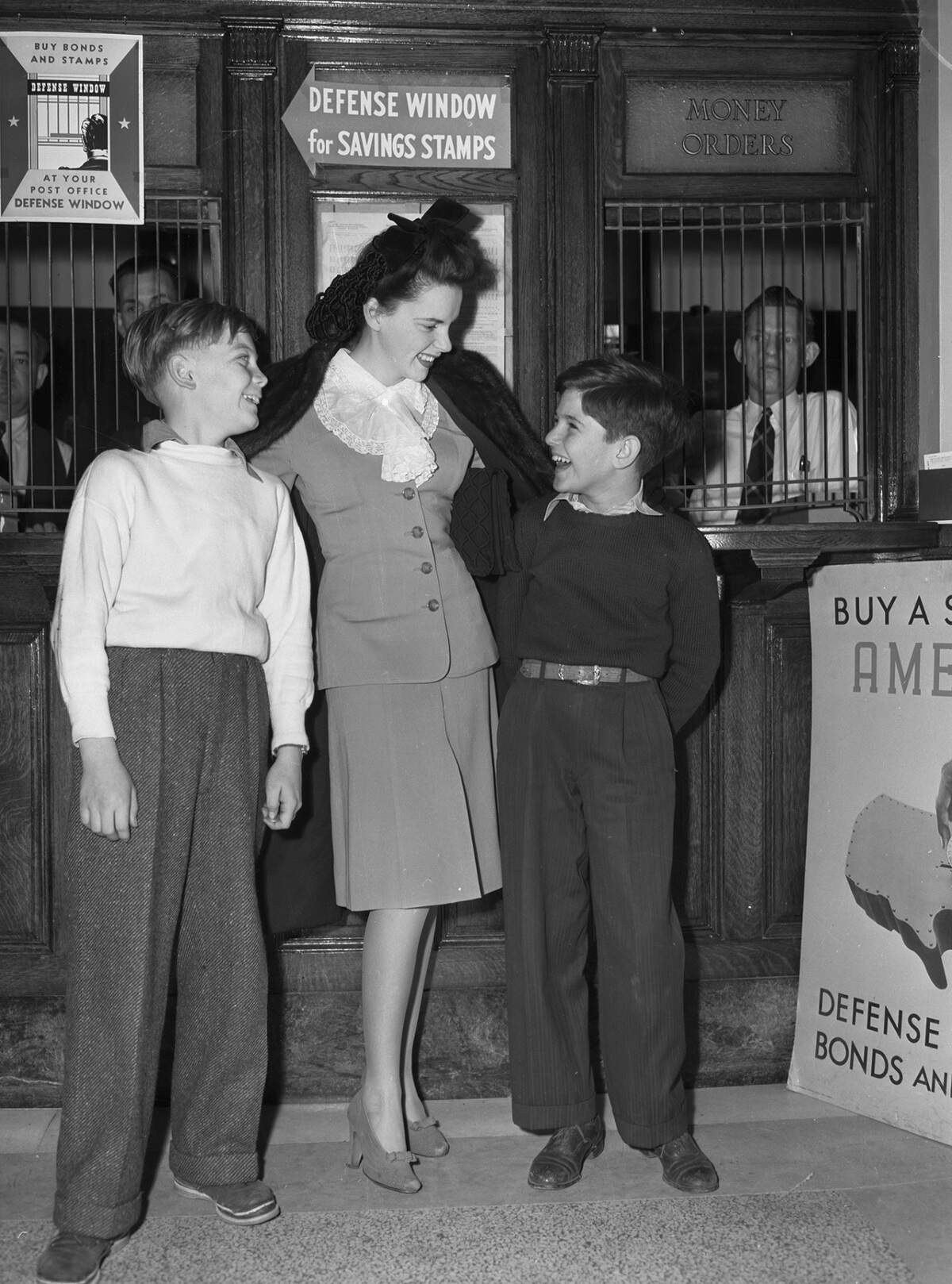 Garland is wearing a bow in her hair, a suit with lace around the collar, and a fur jacket over her shoulders. Billy is wearing a sweater and trousers. Herbert is dressed in a collared shirt, sweater, and trousers. 