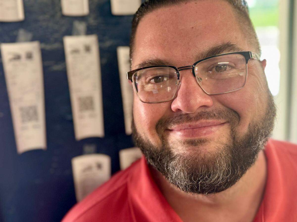 Jeremy Lowe in front of the wall showing pre-paid burgers free to people in need at Nearly Famous Burgers and Hot Dogs in Arlington, May 21, 2024.