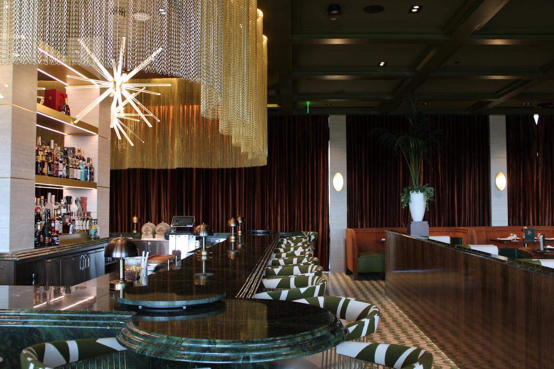 The green marble bar is offset with a sparkling gold chain chandelier, that rims the entirety of the space.