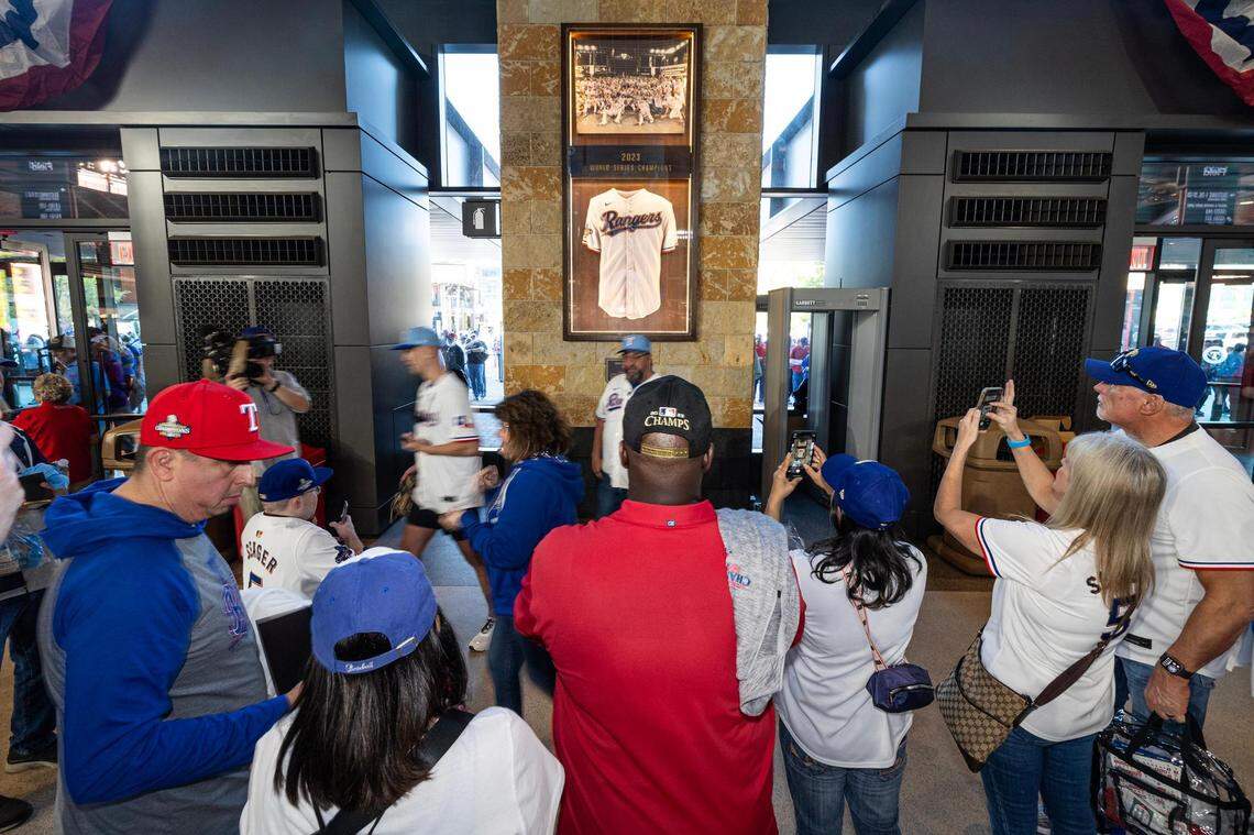 Texas Rangers fans take photos with the 2023 World Series commemorative plaque as they enter the stadium for the 2024 season opener between the Rangers and the Chicago Cubs at Globe Life Field in Arlington on Thursday, March 28, 2024.