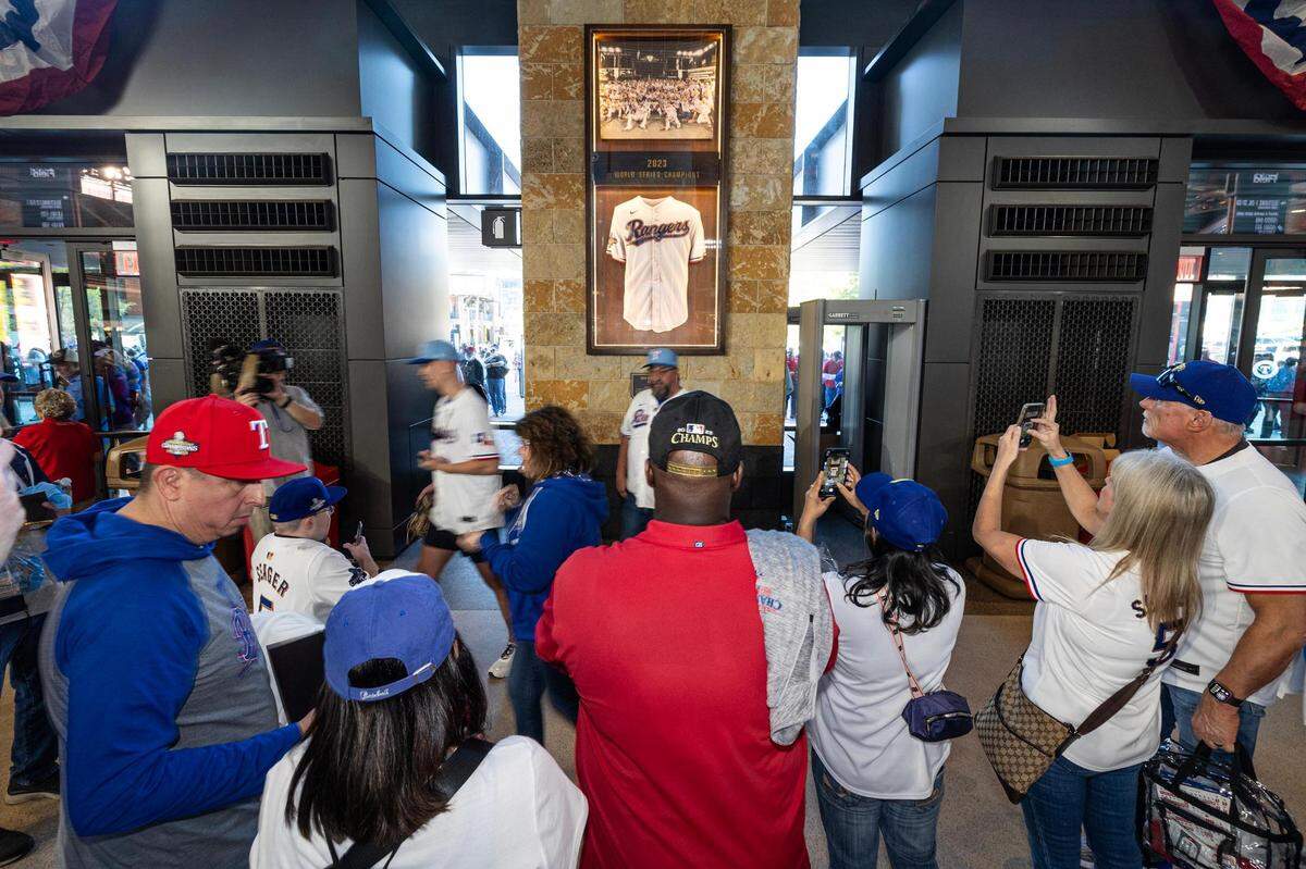 Texas Rangers fans take photos with the 2023 World Series commemorative plaque as they enter the stadium for the 2024 season opener between the Rangers and the Chicago Cubs at Globe Life Field in Arlington on Thursday, March 28, 2024.
