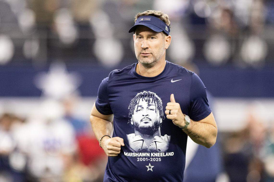 Cowboys Head Coach Brian Schottenheimer hypes up the players prior to the first half of an NFL game between the Dallas Cowboys and the Philadelphia Eagles at AT&T Stadium in Arlington on Sunday, Nov. 23, 2025. Schottenheimer is wearing a shirt in honor of the late Cowboys player Marshawn Kneeland.