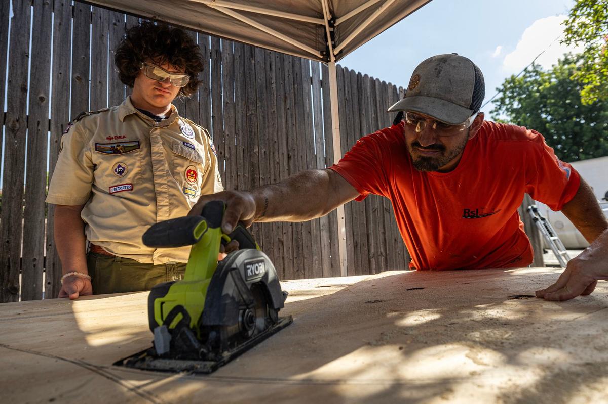 Boy Scout Reese Hughes, left, watches as his brother in law Allen Williams uses a power saw to cut out the new roof of the Bedford well for his Eagle Scout project.