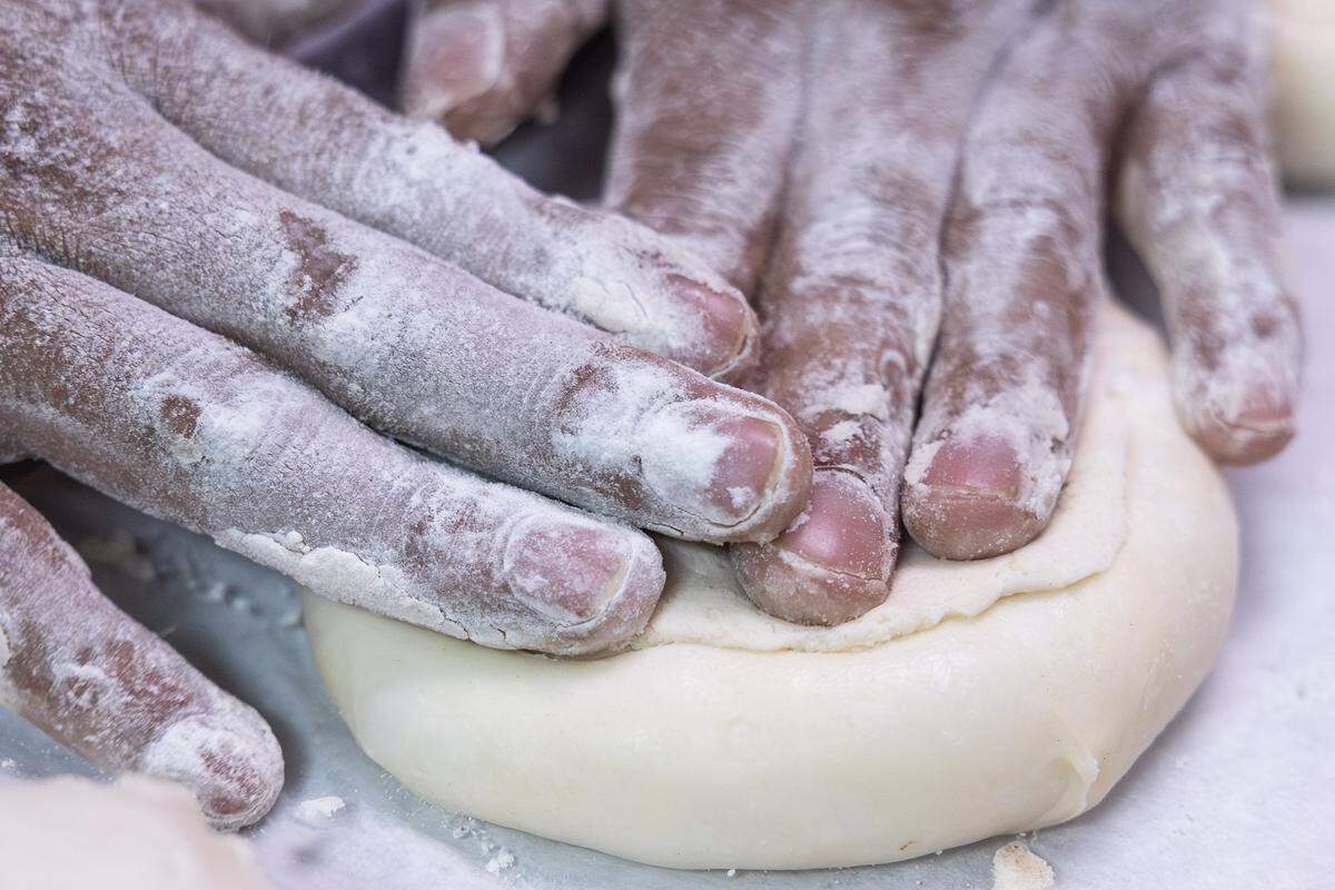 Flour covered hands press down to flatten a ball of dough.