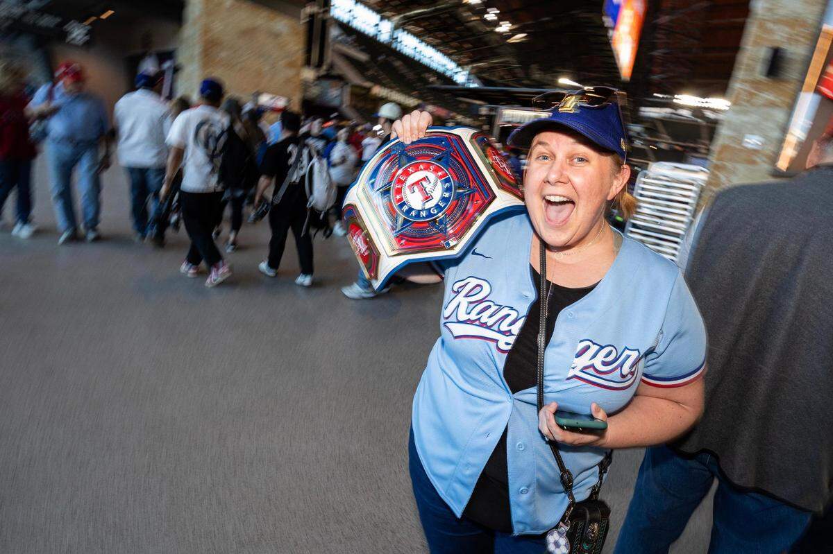 Roanoke resident Jenifer Watson cheers as she holds her custom-made Texas Rangers championship belt for the 2024 season opener between the Rangers and the Chicago Cubs at Globe Life Field in Arlington on Thursday, March 28, 2024.