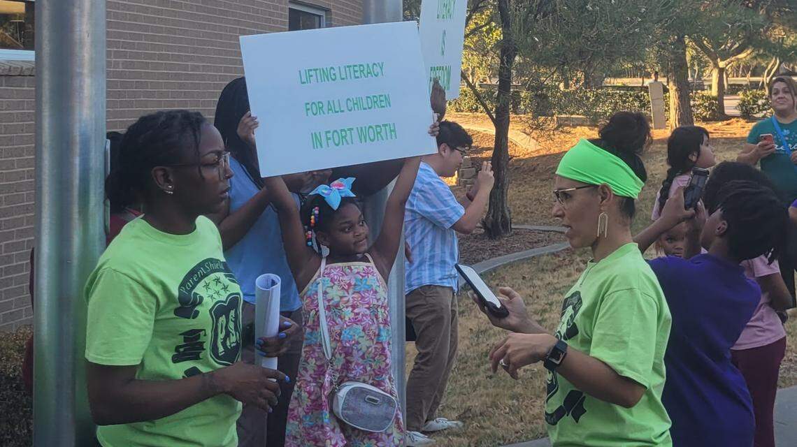 A girl in a flowery jumper holds a sign reading "Lifting literacy for all children in Fort Worth."
