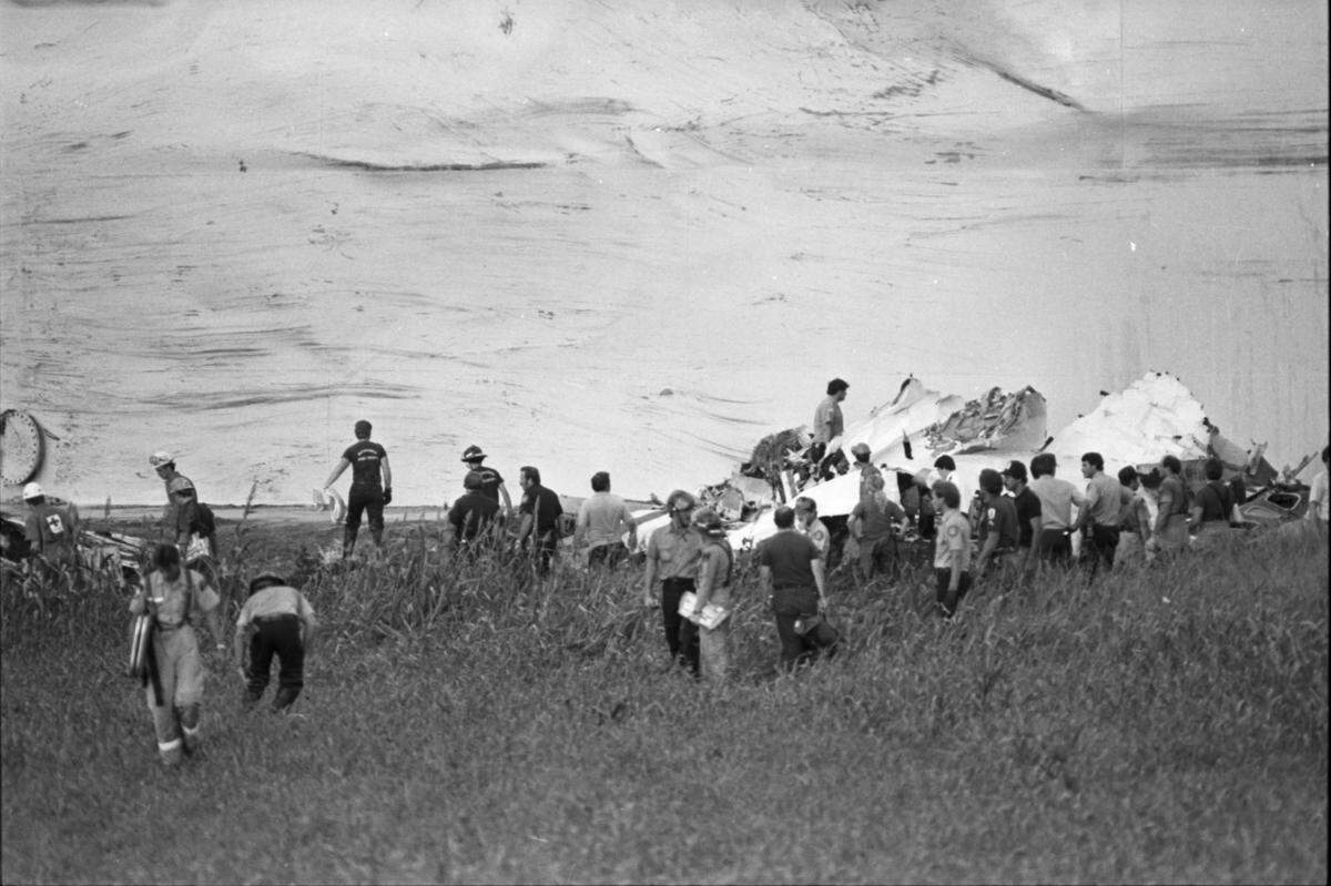 Black and white photo taken from a distance that shows people swarming the wreckage of the plane in a field.