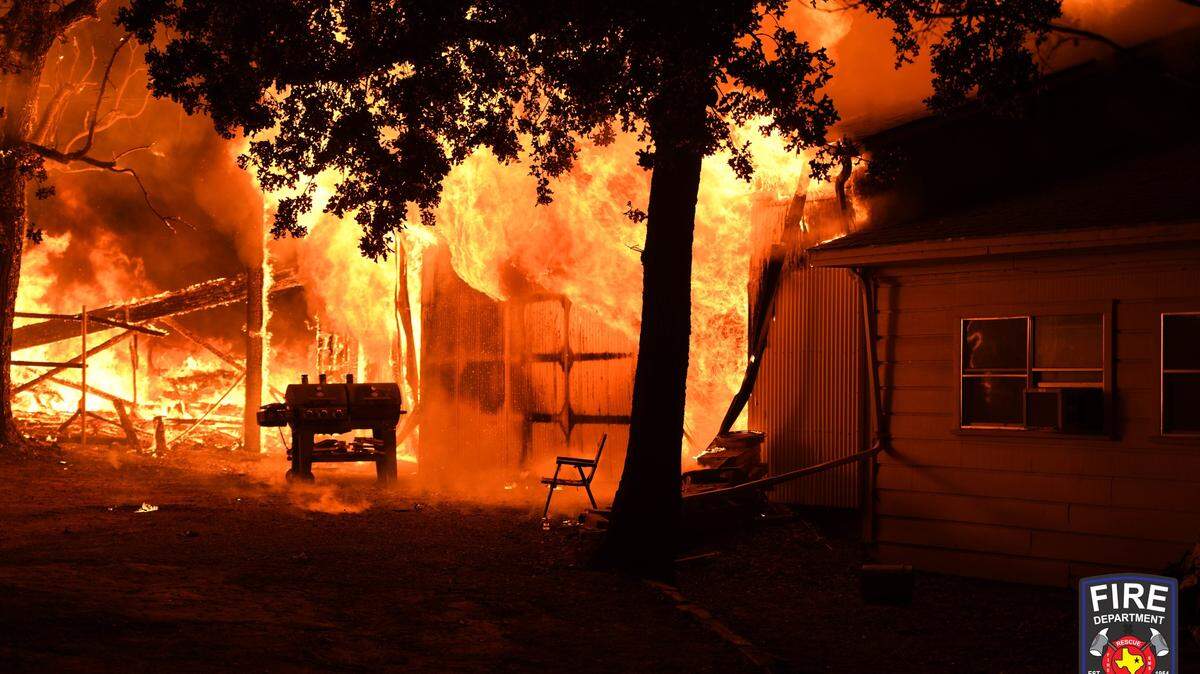 Flames billow out of a structure in Bedford, Texas. A house is in front of it.