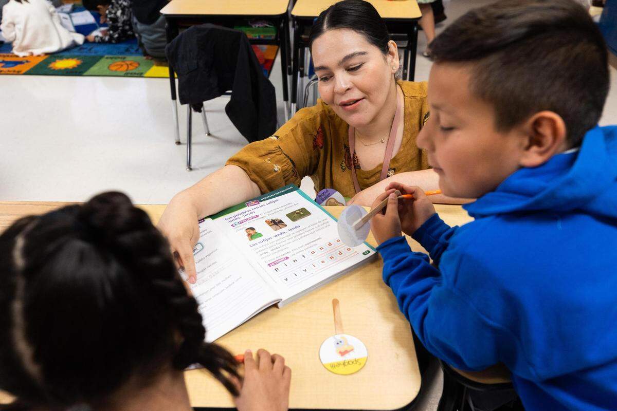 Teacher Maria Andrade helps Nicholas Lugo and Alayna Suarez with work during a second grade bilingual class at M. H. Moore Elementary in Fort Worth.
