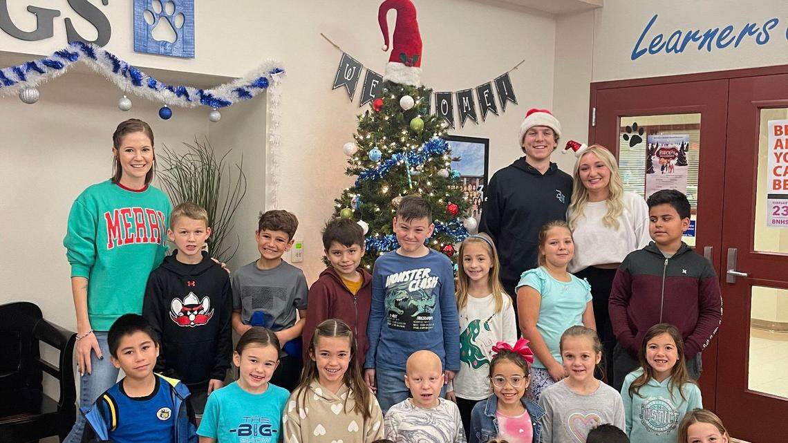 Madaleine Murphy (white shirt in back) and Sebastian Kravutske (in hat) share some time with students at Samuel Beck Elementary after delivering messages from an Elf On a Shelf. The Byron Nelson High School seniors created a charitable organization named Miracle of Kindness that sends handmade inspirational cards to people.