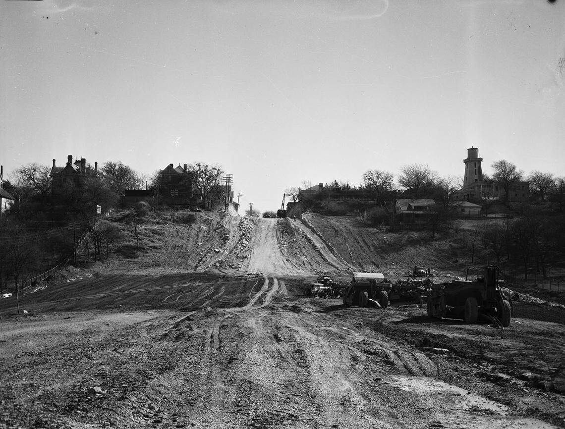 Jan. 24, 1942: View of improvement and construction work being done on West Lancaster Avenue in Fort Worth, Texas. Automobiles, tractors and other machinery are shown on the dirt road at the right. In the background are various buildings.
