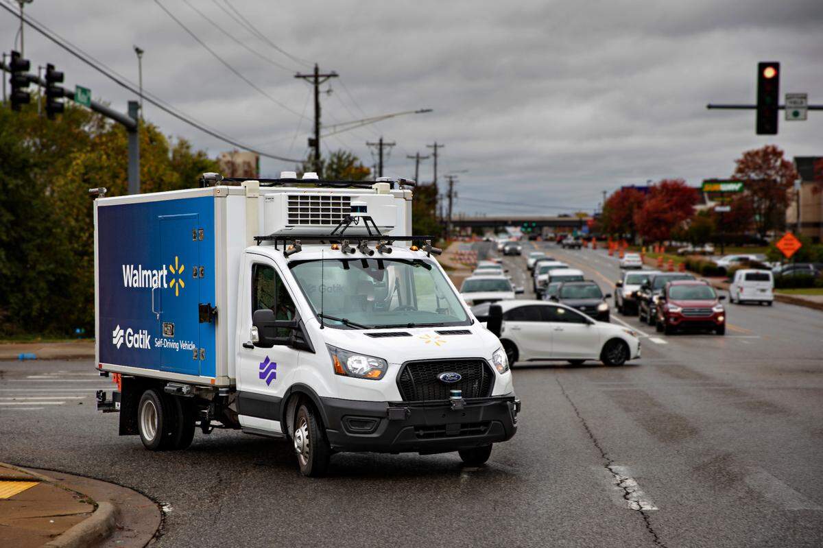 A four-wheel autonomous delivery truck crosses an intersection full of cars without any driver in the front seat.