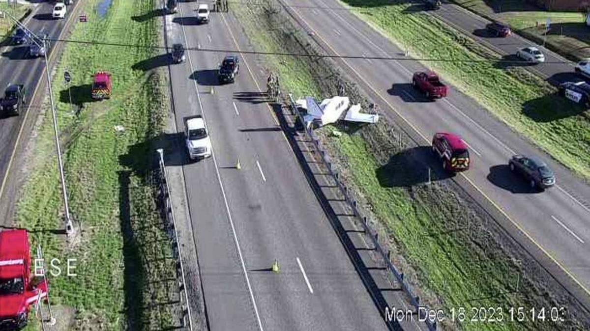 An image from a traffic camera shows a small airplane in the grassy median very close to a highway.
