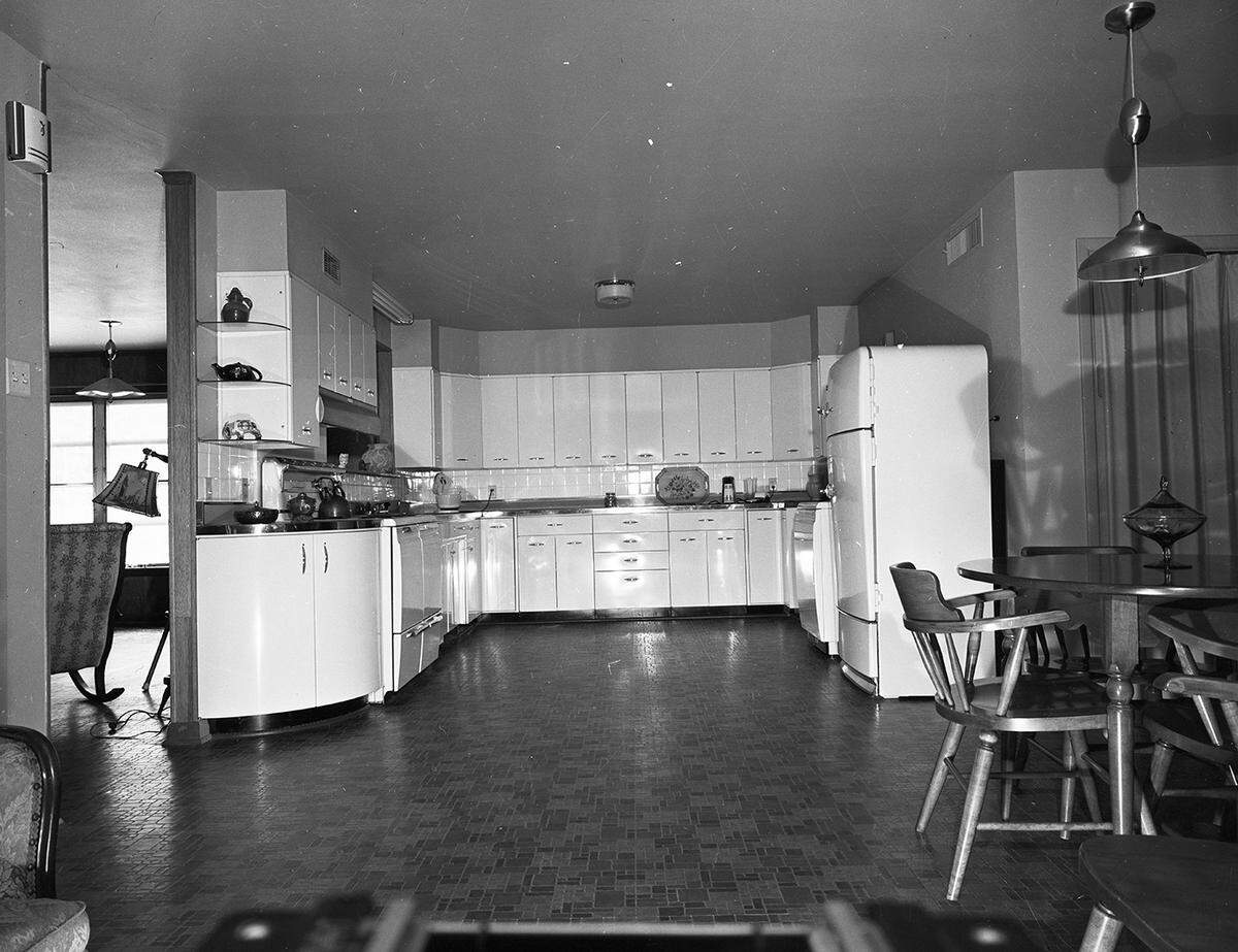 April 1954: The white kitchen end of an all purpose room in the new home of Miss Mavis Douglas, 2700 Colonial Parkway. The floor is covered with broken tile pattern of linoleum. Custom made cabinets and appliances line the wall on three sides.