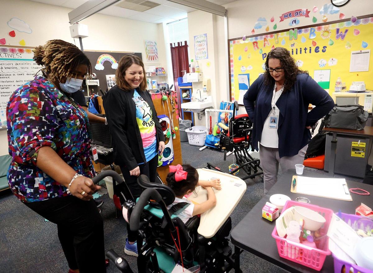 Superintendent Ramsey stands while talking to a young student in a wheelchair in a colorful classroom.