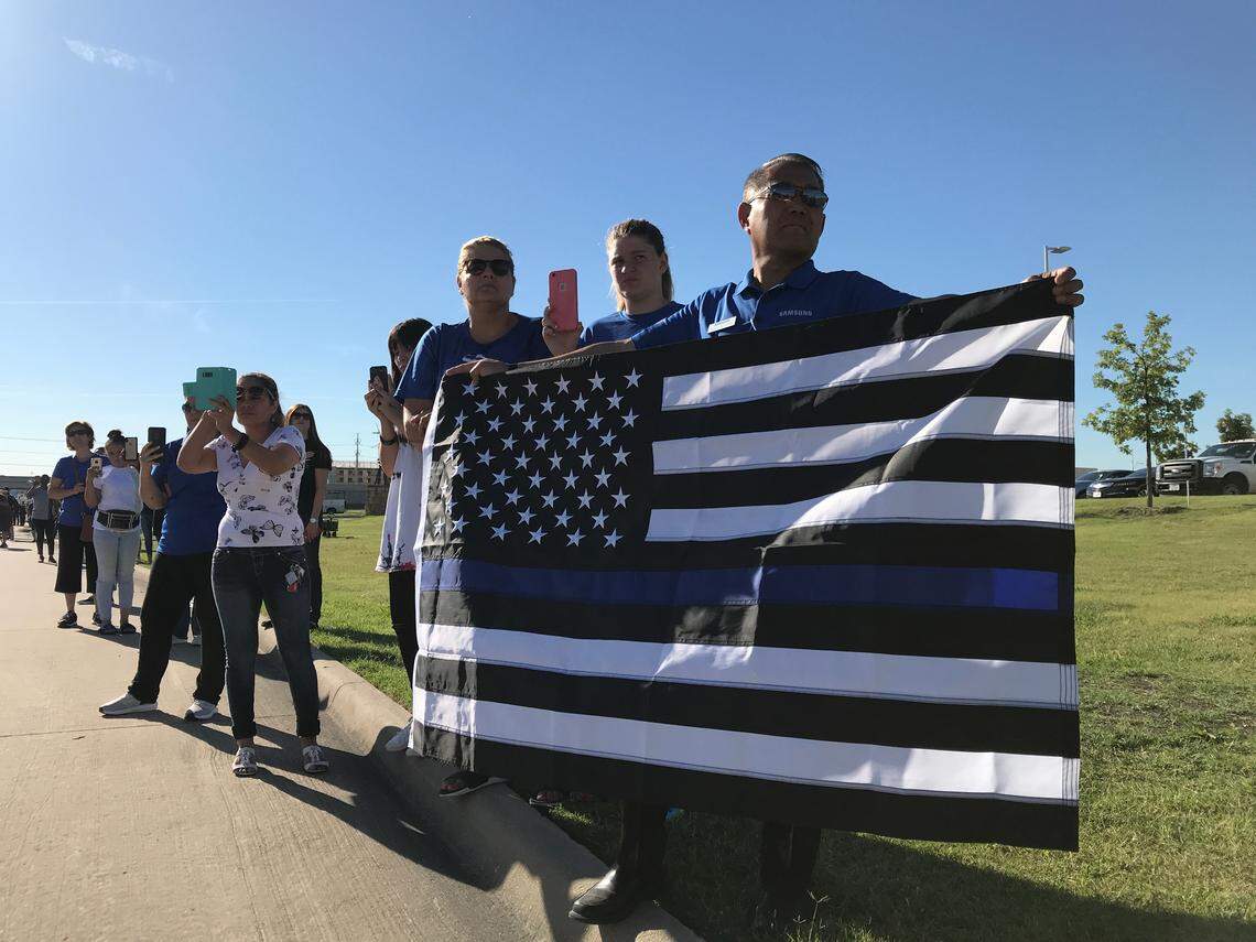 Takamasa Kamo (right) holds out an American flag in front of the Grand Prairie Public Safety Building as a processional carrying fallen Grand Prairie Officer AJ Castaneda’s body passed by. He said he came before his job at Samsung began.