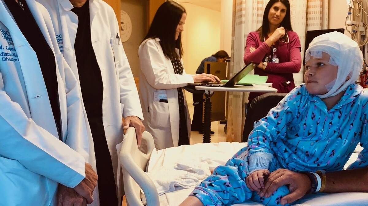 A girl on a hospital bed, her head wrapped in bandages, talking to doctors.