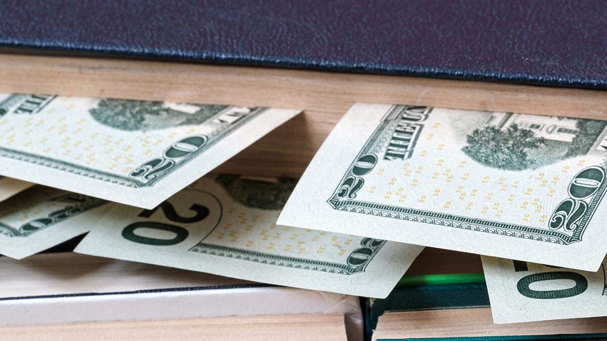 full of money sticking out of the pages of a book laying on other books standing upright, if you read the book to find out where to get the money
