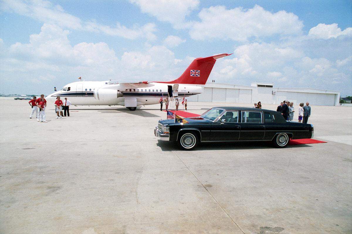A black Cadillac limo carrying Queen Elizabeth at Love Field Airport, with a red carpet that extends to a jet parked on the runway. Two boy scouts are seen at the stairs to the plane, one is holding an American flag while the other is holding a British flag.