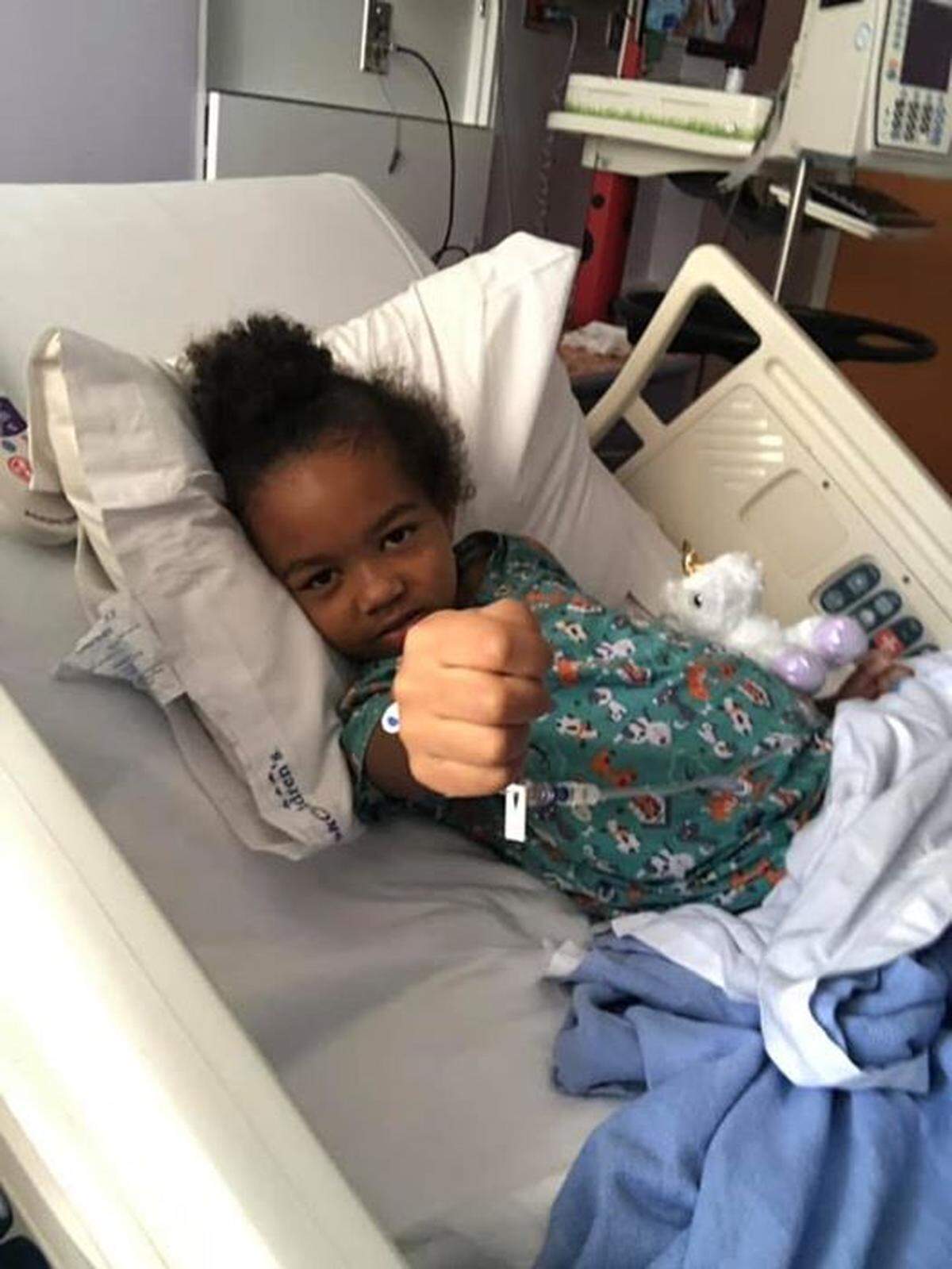 Adriana Nixon, 6, outstretches her fist as she lies in a hospital bed. She was diagnosed with a rare cancer in her liver in June 2019.