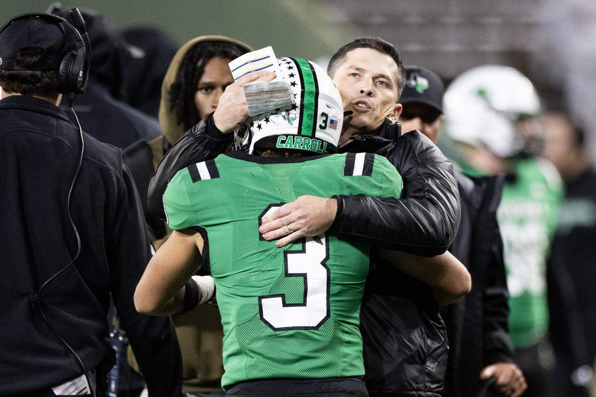 Southlake Carroll head coach Riley Dodge hugs running back Davis Penn (3) on the sidelines after scoring a touchdown in the second half of the UIL Division II Regional playoff game at Choctaw Stadium in Arlington on Friday, Nov. 28, 2025.