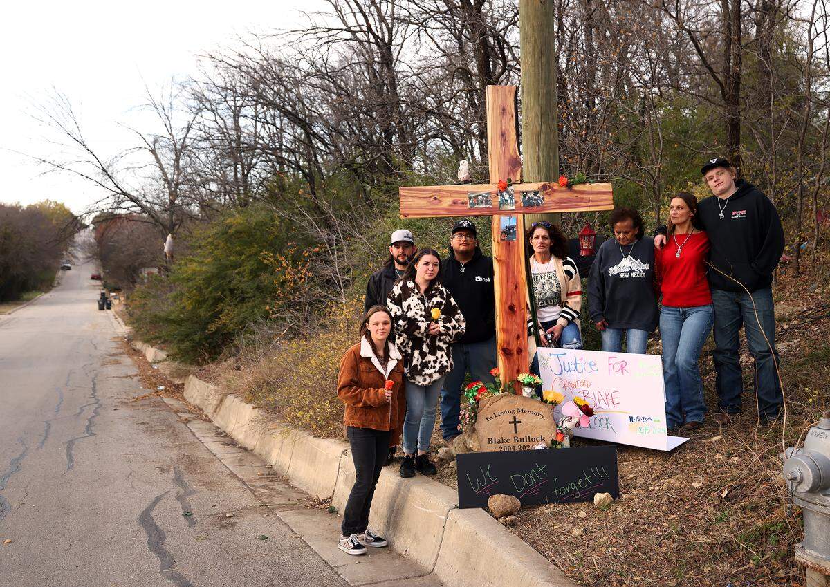Family and friends stand beside a large wooden cross marking the area where Blake Bullock was found lying in the street after being struck by a police vehicle responding to a report of gunfire.