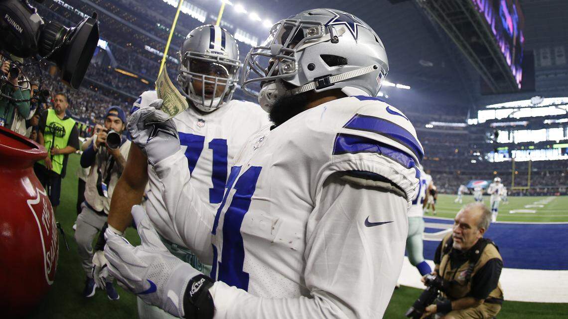Dallas Cowboys running back Ezekiel Elliott pulls out a twenty and a dollar bill to put in the Salvation Army kettle after scoring a touchdown against the Washington Redskins on Thursday.