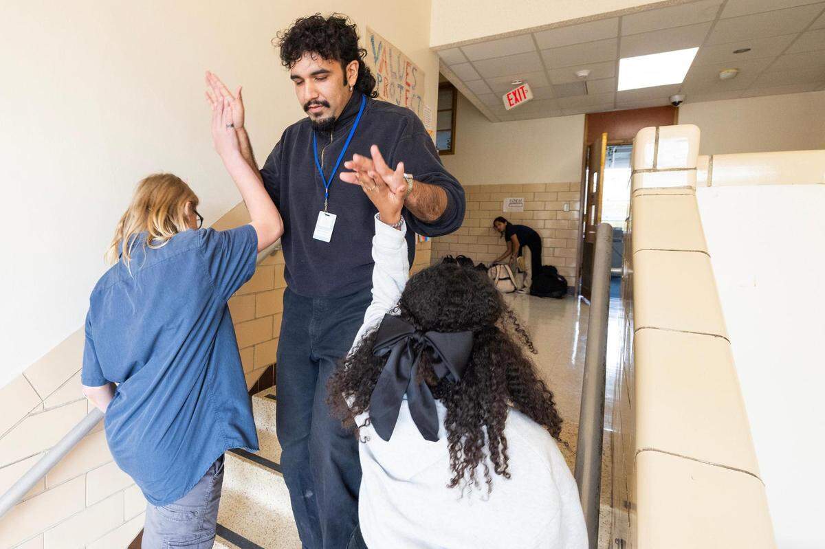 Omar Marquez, a restorative practices coach, gives a high five to Noah Lane, 12, and Lyla Vanderstole, 14, as they head to his classroom to resolve a conflict at Applied Learning Academy in Fort Worth on Wednesday, Nov. 29, 2023.
