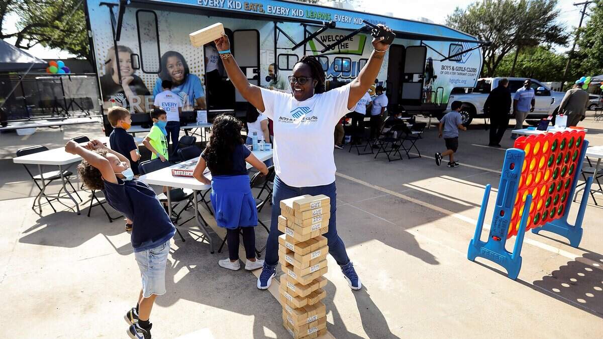Shakia Jackson-Williams, assistant manager of the East Side Boys & Girls Club, celebrates a successful pull of a giant Jenga block with Boys & Girls Club member Aiden, 7, during an unveiling of the new Mobile Clubhouse Experience in 2021 in Fort Worth. The Mobile Clubhouse is composed of a fleet of vehicles, including the flagship RV, that can be unpacked to bring services, as seen, directly to communities.