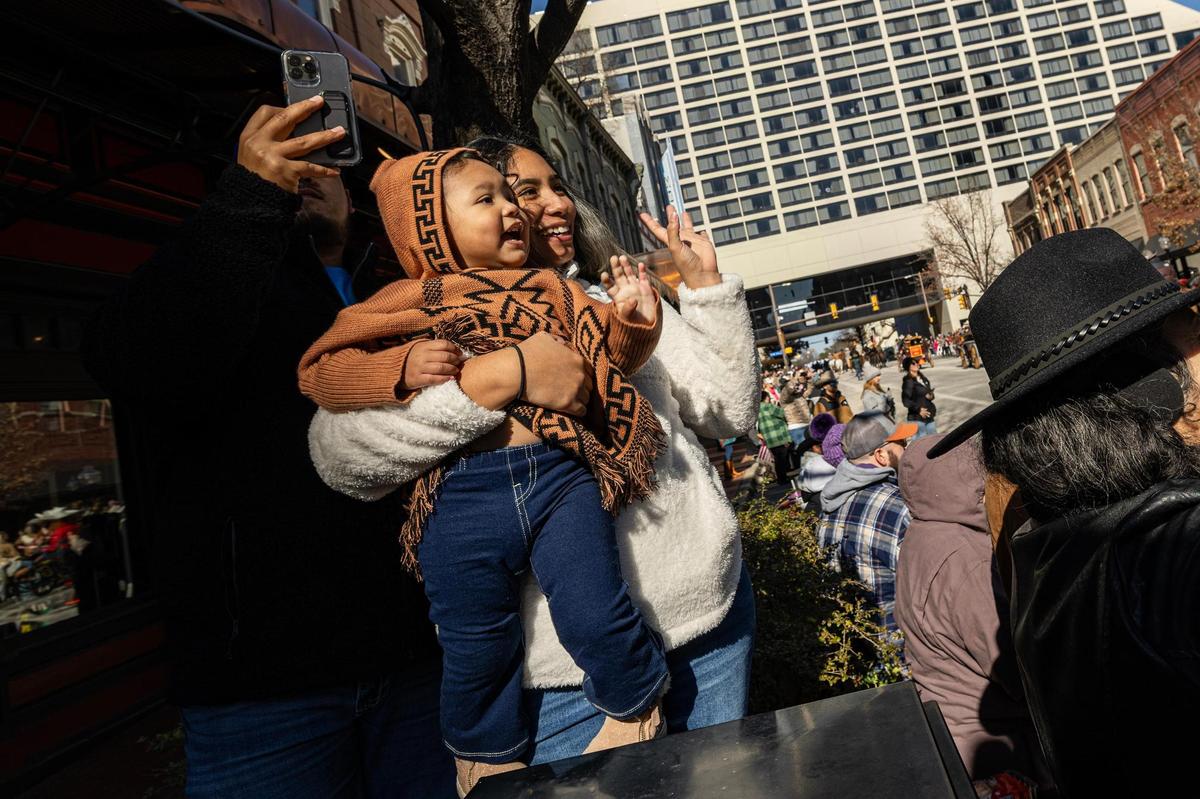Gina Escobedo and her daughter Emely, 2, wave at the wagons and floats making their way down Houston Street during the Fort Worth Stock Show All Western Parade in downtown Fort Worth on Saturday, Jan. 18, 2025.