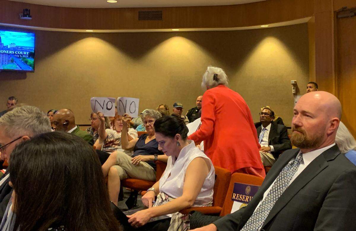 Three Tarrant County residents held up signs saying “NO” as the commissioners court voted along party lines to hire Public Interest Legal Foundation as its legal representation in the redistricting lawsuit.