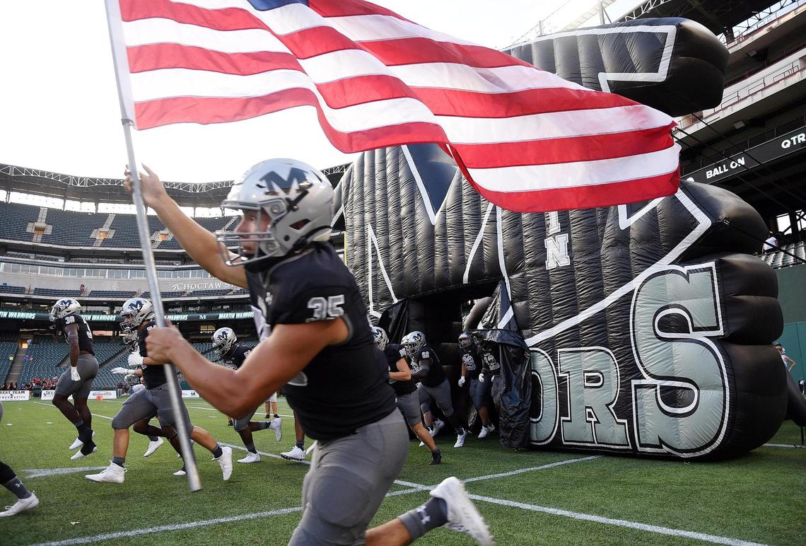 Arlington Martin’s Aaron Martinez front, runs with the American Flag as the Warriors take the field to play Lake Travis. Martin won 39-31.