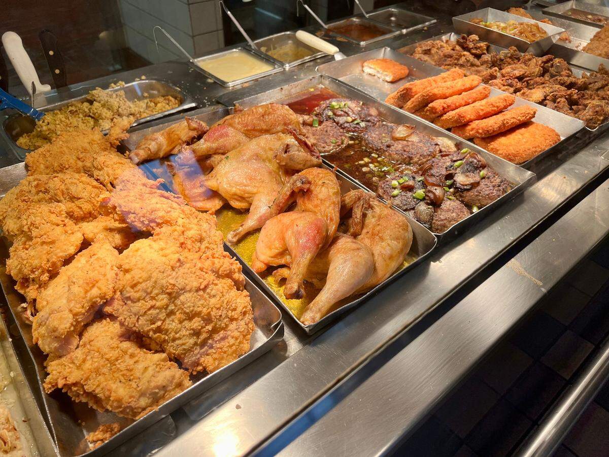 Cafeteria serving line loaded with fried chicken and other entrees under sun lamps.