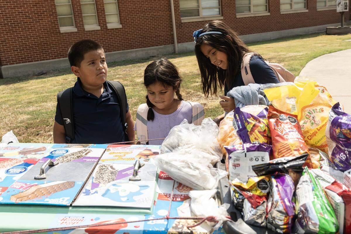 Siblings Cameron, 8, Carolina, 6, and Camila Olivas, 9, select which ice cream they want from the ice cream man after school gets out at Riverside Applied Learning Center in Fort Worth on Tuesday, Aug. 19, 2025.