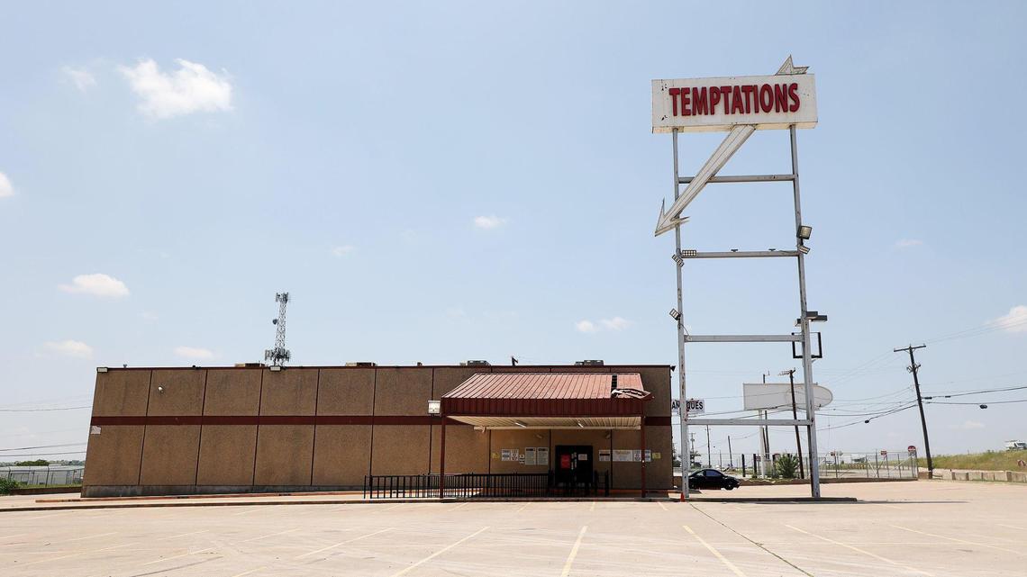 A white sign that reads "Temptations' points down towards a square brick building.