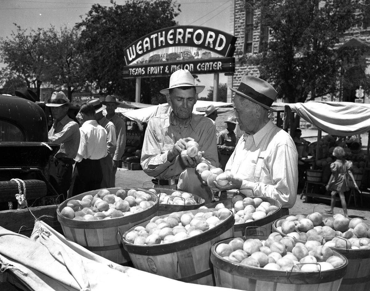 July 8, 1939: At Trading Day in Weatherford, Texas. G.A. Holland (right), Weatherford banker and former mayor, inspects Hart cling peaches being sold by J.A. Melton, who owns an orchard 11 miles northwest of town.