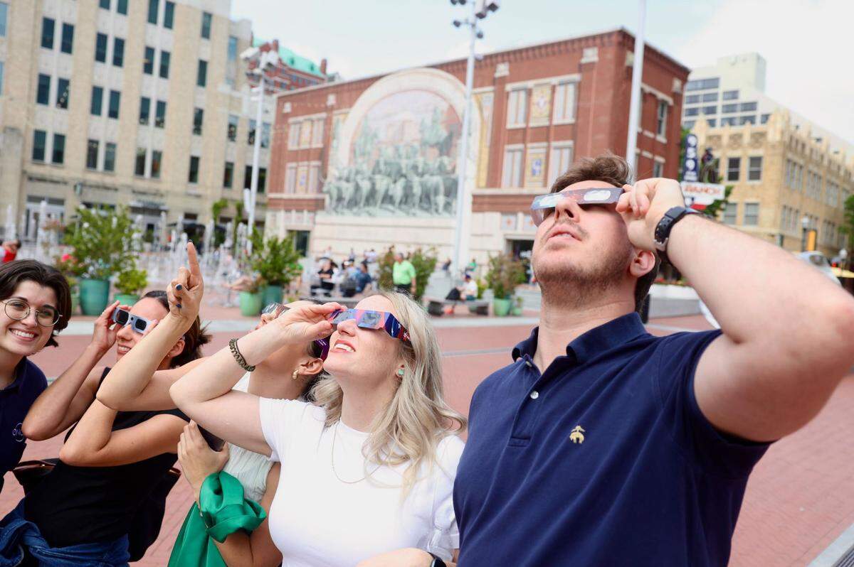 Five people wearing special eclipse glasses stare up at the sky.