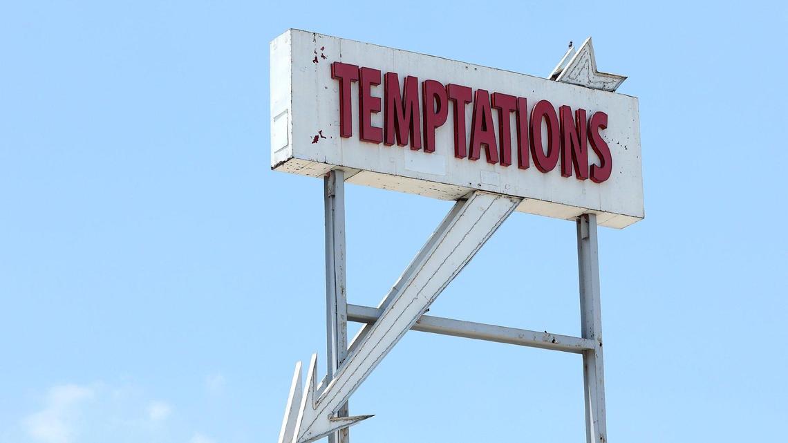 A large white sign has Temptations in red lettering. An arrow comes from the bottom of the sign on a diagonal pointing down.