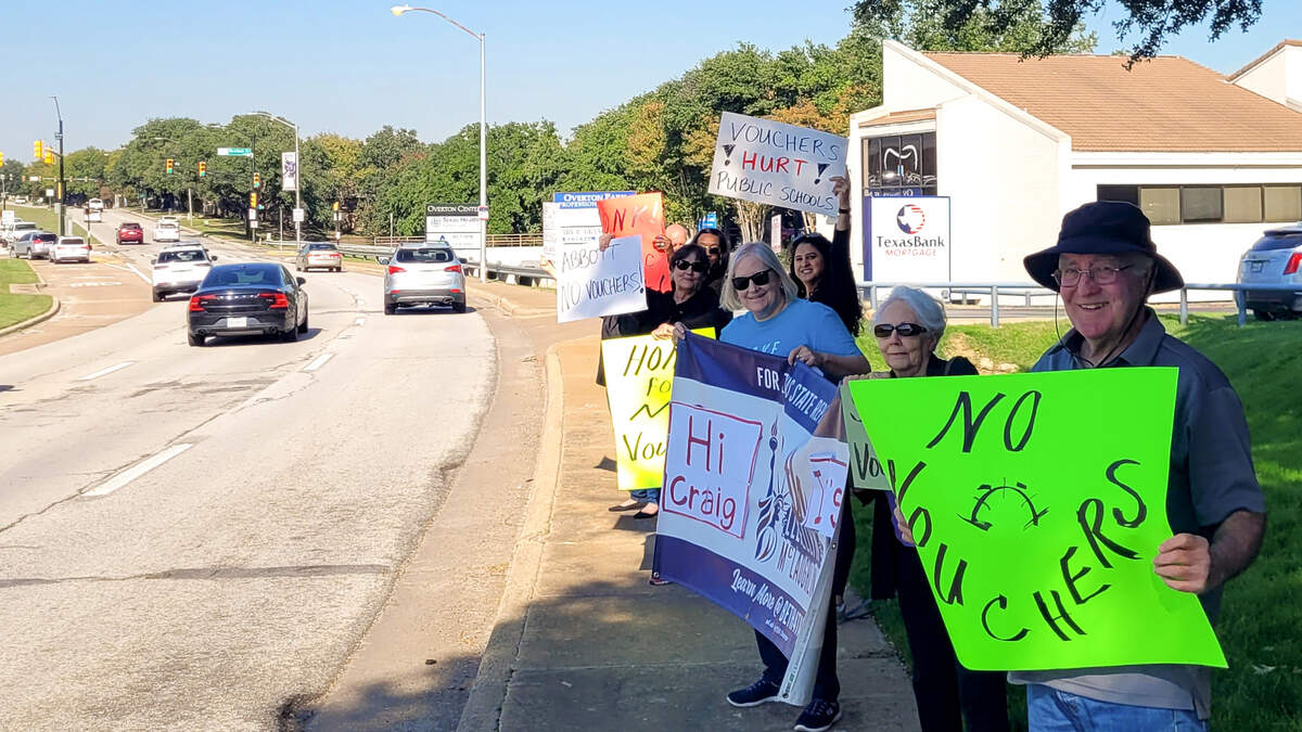 People stand with signs on a four-lane road. 