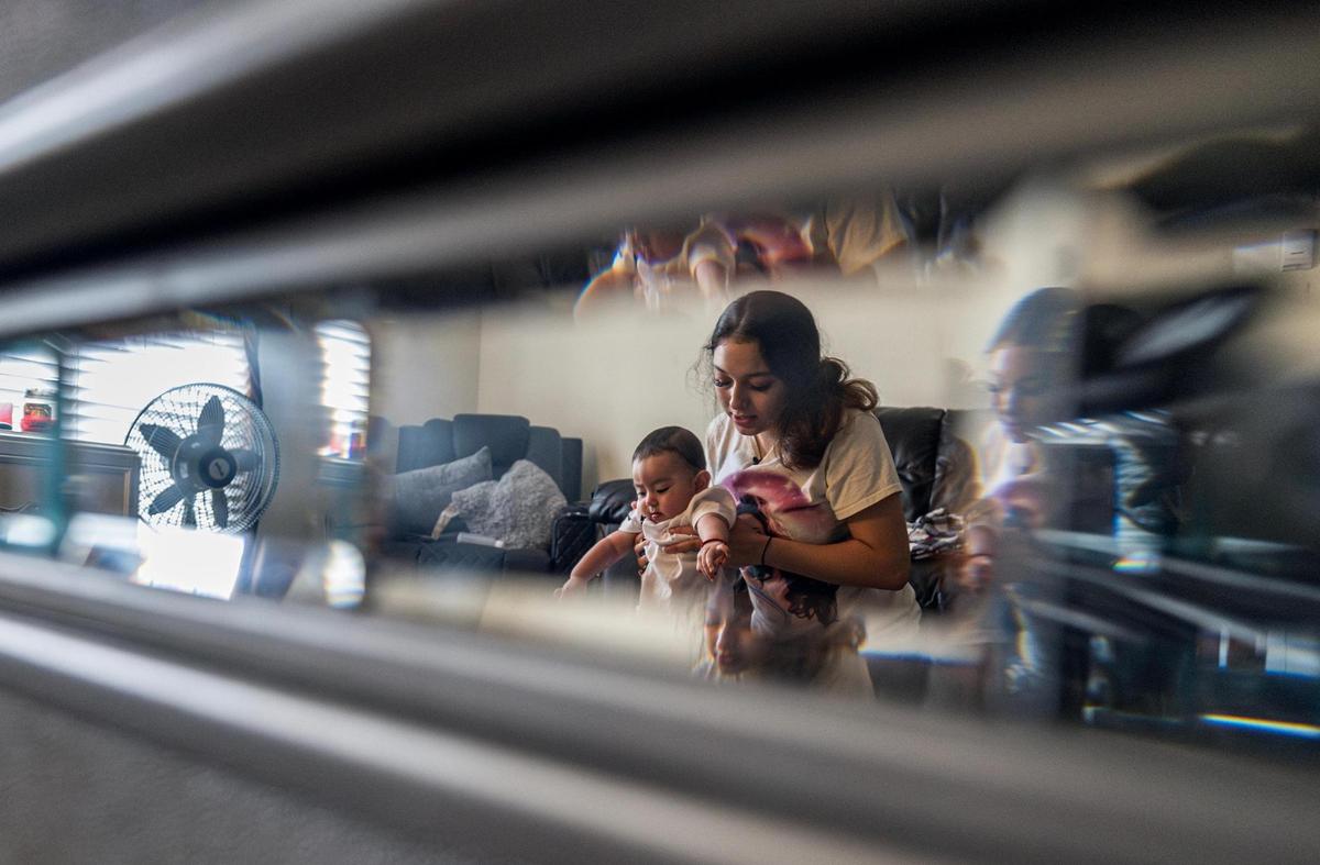 Corina Camacho is reflected in glass as she plays with her son at her apartment in Fort Worth. Camacho said she cannot forgive the teen boys who shot the child’s father and his cousin.