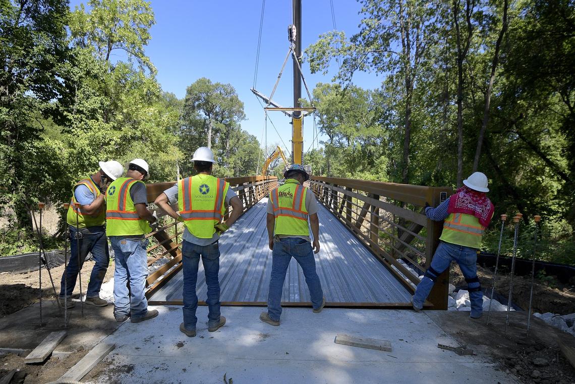 A crane drops a pedestrian bridge into place while crews help on Thursday along the River Legacy Trails in Arlington.